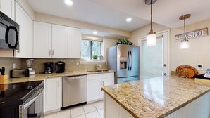 Eine moderne Küche mit weißen Schränken, Granit Arbeitsplatten, einem eingebauten Backofen, einem Kühlschrank und einem Fenster mit Blick auf Bäume.