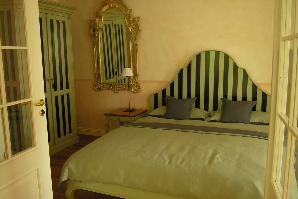 Une chambre à coucher avec un lit, une table de chevet, une lampe, un miroir et une porte.