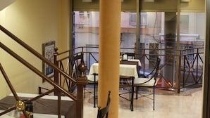 Um hall de hotel com escadaria, um pilar grande e vista para o exterior através de uma porta de vidro.