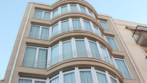 Um hotel com vários andares, fachada curva, grandes janelas com molduras brancas e varandas nos andares superiores.
