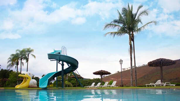 Una piscina con scivolo, sdraio, palme e un lampione.