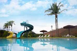 A swimming pool with a water slide, lounge chairs, palm trees, and a lamp post. - Hotel Serraverde (Pouso Alto)