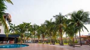 A pool area with palm trees, outdoor seating, and a building with a bar. - Francis Hotel (Abuja)