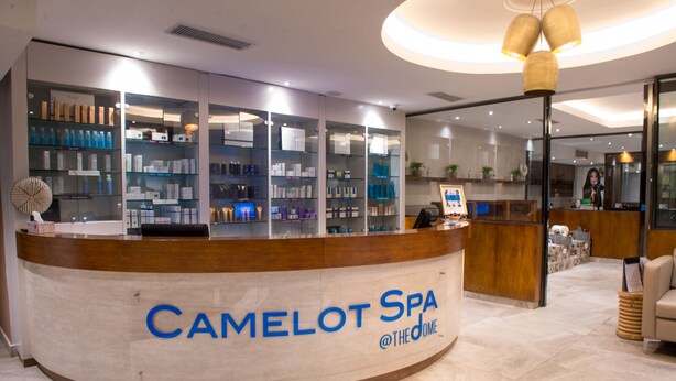 A reception area with a counter labeled "CAMELOT SPA @THE DOME" and shelves displaying various products. - Francis Hotel (Abuja)