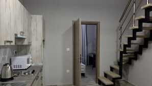 Une cuisine compacte équipée d’un four à micro-ondes, d’une bouilloire et d’une machine à café, le tout posé sur le plan de travail. Un escalier en bois mène à une chambre  à coucher comprenant un lit et une table de chevet.
