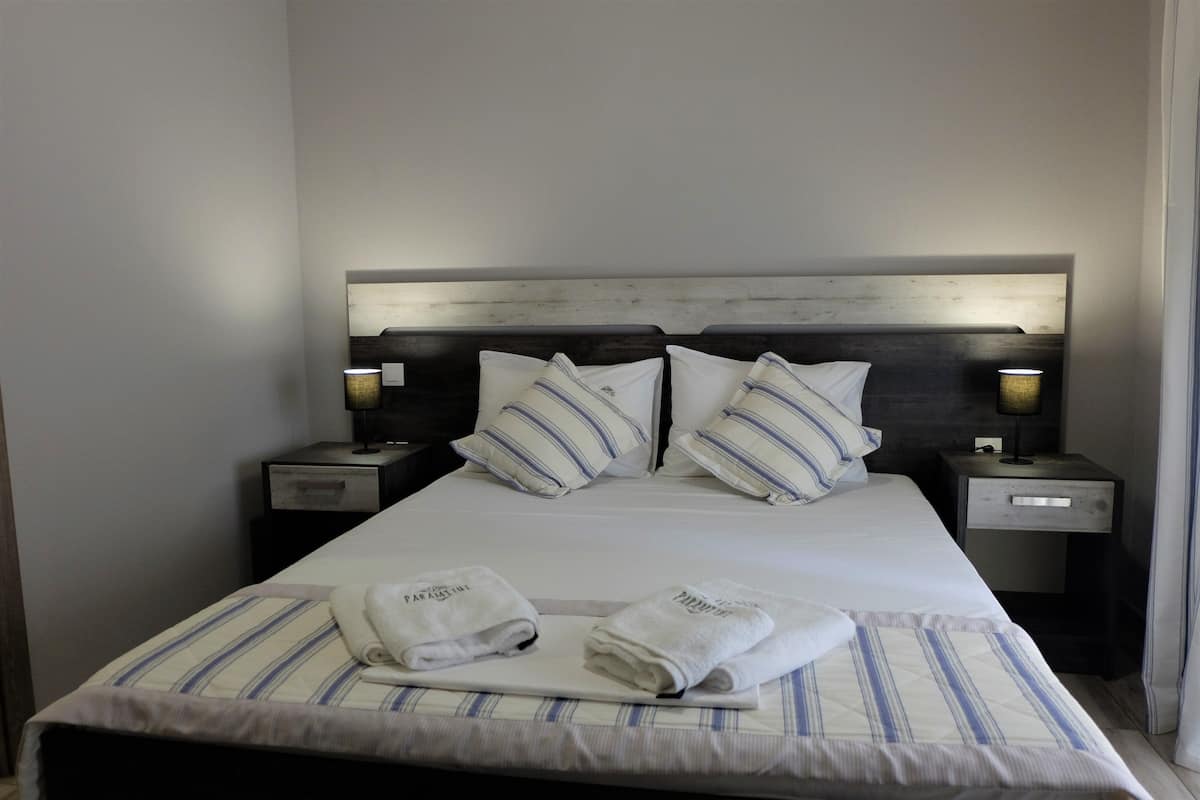 A neatly made bed with striped bedding, two pillows, two bedside lamps, and two folded towels on the bed.