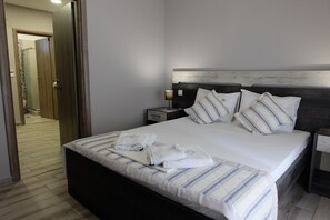 Uma cama bem arrumada com roupa de cama listrada, uma cabeceira de madeira e duas mesas de cabeceira com abajures.