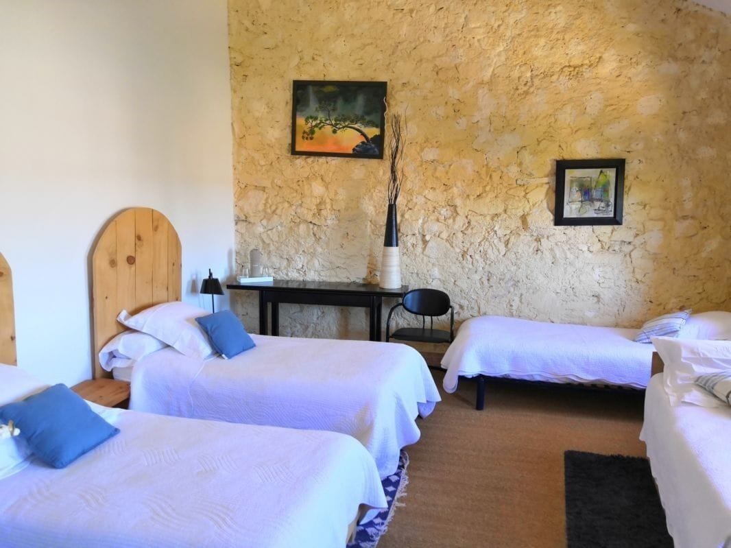 Ein Zimmer mit vier Betten, einem Holzkopfteil, einem Schreibtisch mit Stuhl, einer Vase und zwei Bildern an der Wand.