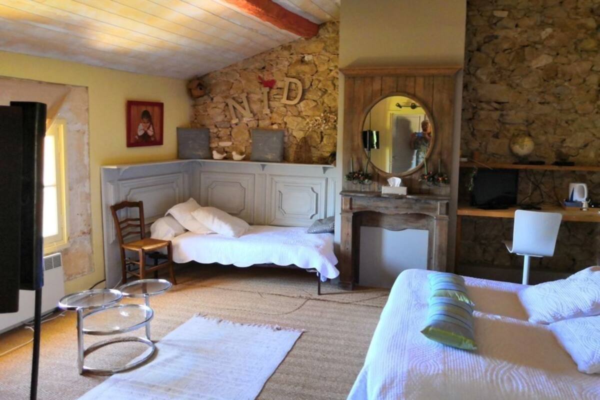 A bedroom with a stone wall, a bed with white bedding, a wooden chair, a small round table, and a mirror.