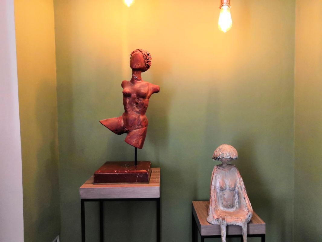 Two sculptures on pedestals against a green wall.