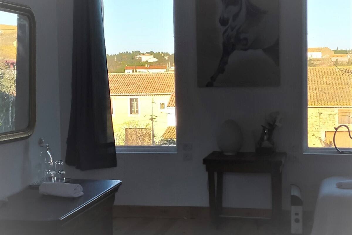 A room with a large window, a painting of a horse, a small table, and a chair.