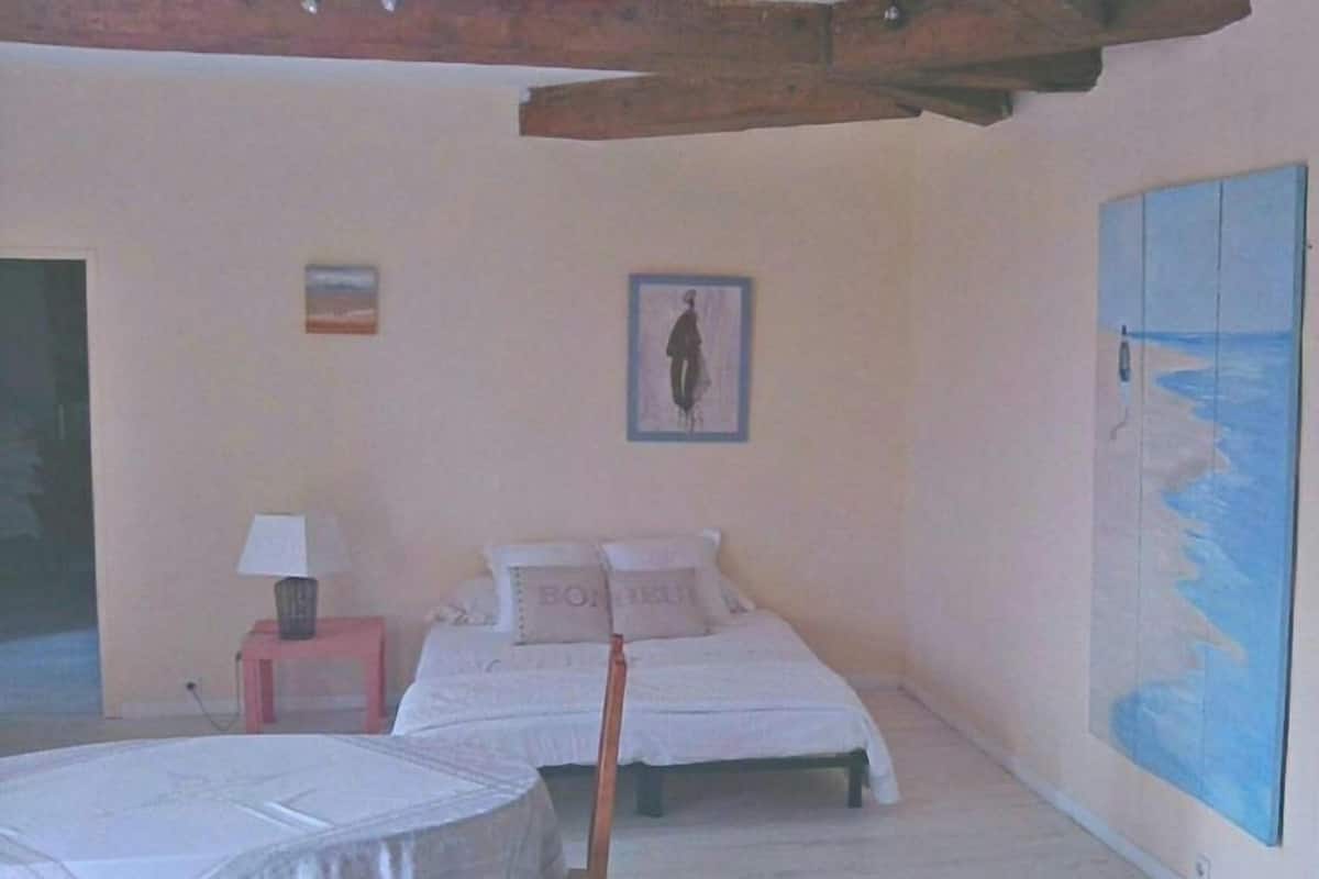 A bedroom with two beds, a small table with a lamp, and a large painting of a beach scene.