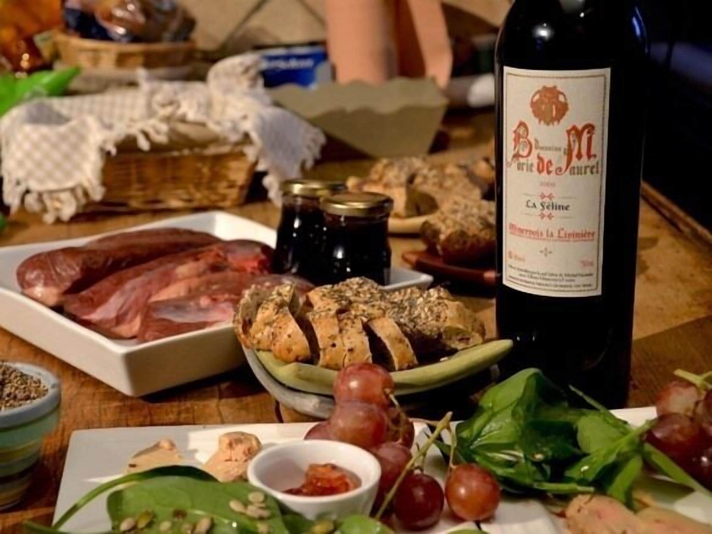 A table with various food items including sliced bread, grapes, and a bottle of wine.