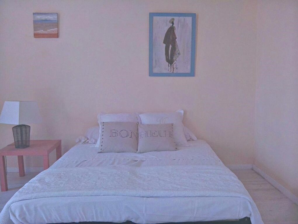 Ein Schlafzimmer mit einem Bett, Kissen, einem Nachttisch, einer Lampe und zwei gerahmten Bildern an der Wand.