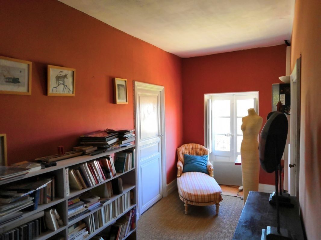 Ein Zimmer mit roter Wand, einer Bücherwand voller Bücher, einem Sessel mit Streifenmuster und einer Mannequin.