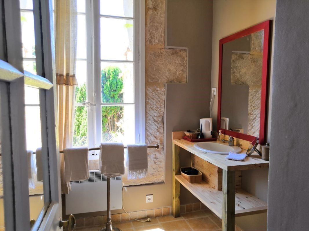 A bathroom with a large window, a wooden vanity, a red-framed mirror, and a towel rack.