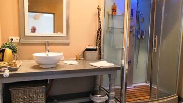 Een badkamer met een wit wastafel, een spiegel, een douche met glazen deuren en een rieten mand.