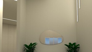 Un área de espera moderna y minimalista con un banco blanco, dos plantas en macetas y un espejo fijado a la pared.