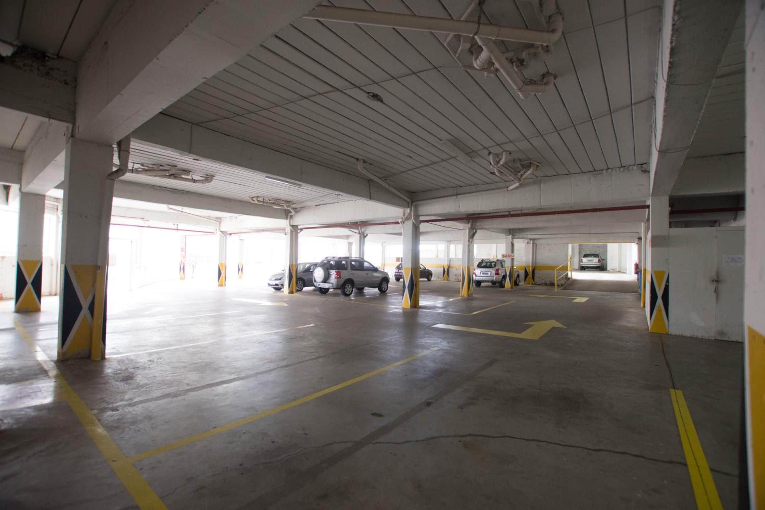 A multi-level parking garage with concrete pillars, yellow directional arrows, and several parked cars.