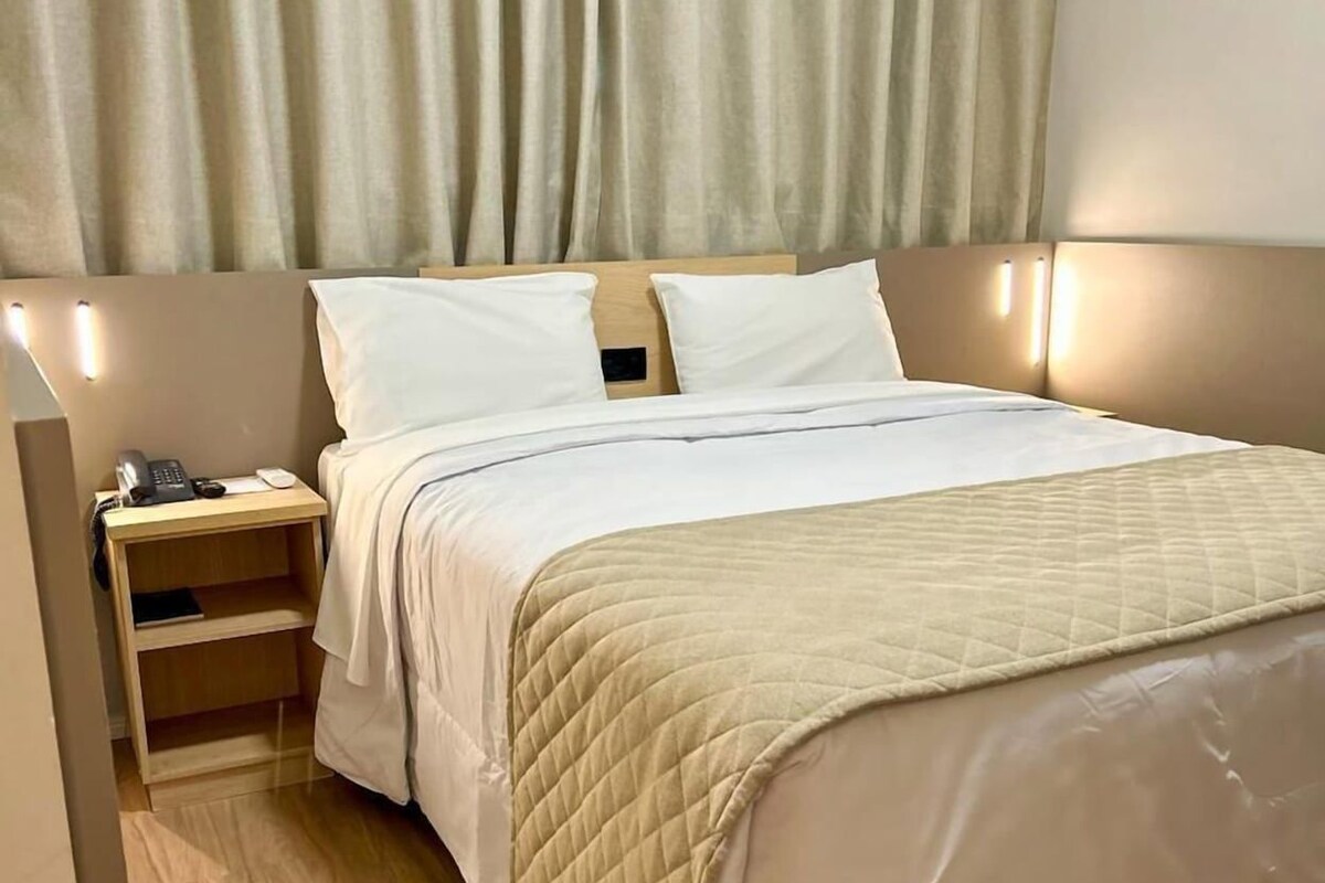 A hotel room with a bed, bedside tables, a nightstand, and a curtain.