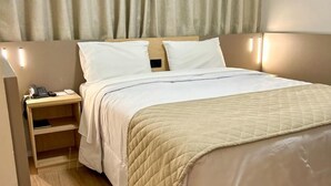 Una cama bien hecha con una colcha acolchada, una mesita de noche con una lámpara y una cortina cubriendo la ventana.