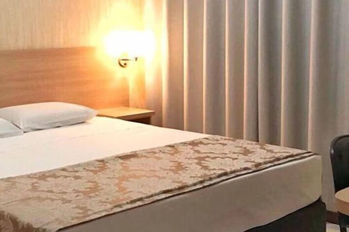 A hotel room with a bed, bedside tables, a telephone, and wall-mounted lights.