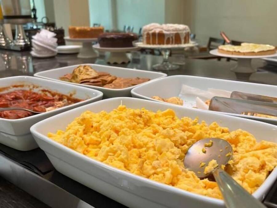 A buffet with various food items including scrambled eggs, pasta, and a cake.