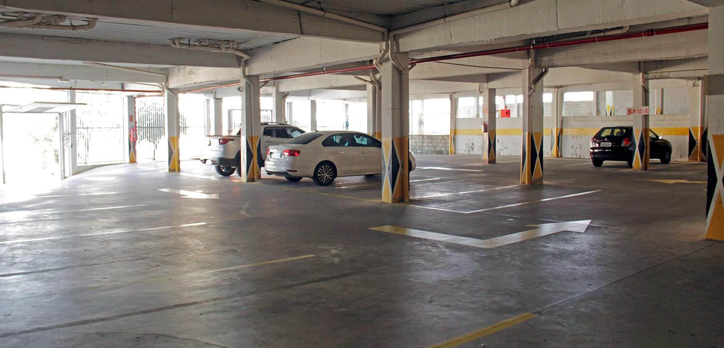 Garagem de estacionamento com vários níveis, pilares de concreto e vagas demarcadas.