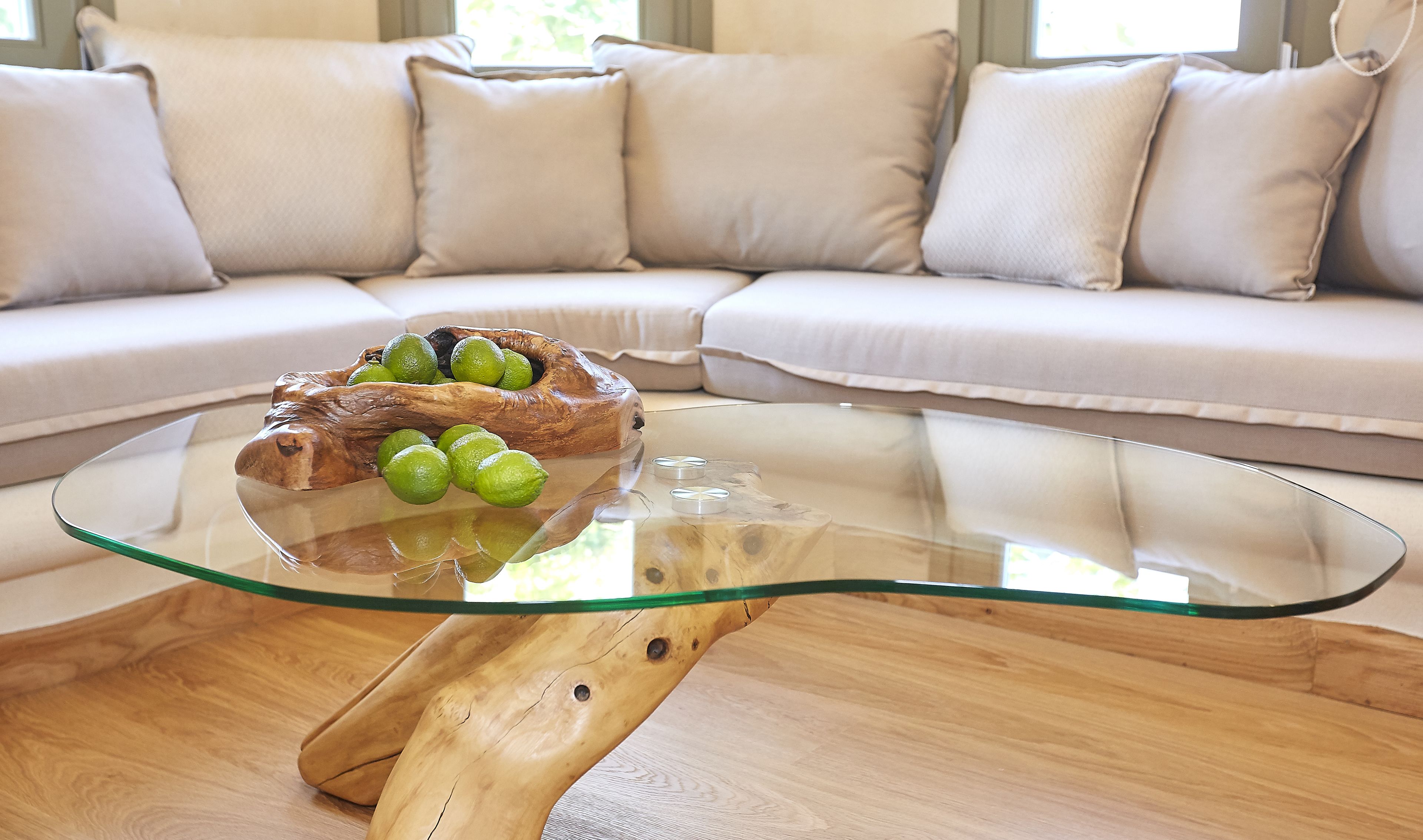 A glass coffee table with a wooden base, a bowl of limes, and a loaf of bread.
