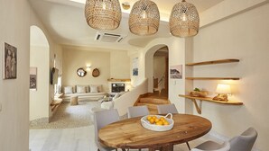 Un vaste espace de vie comprenant une table à manger en bois, des chaises à revêtement gris et un luminaire en fibres tressées.