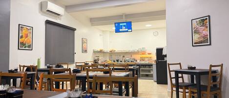 Un restaurante con varias mesas y sillas, un equipo de aire acondicionado y una pantalla digital con el menú.