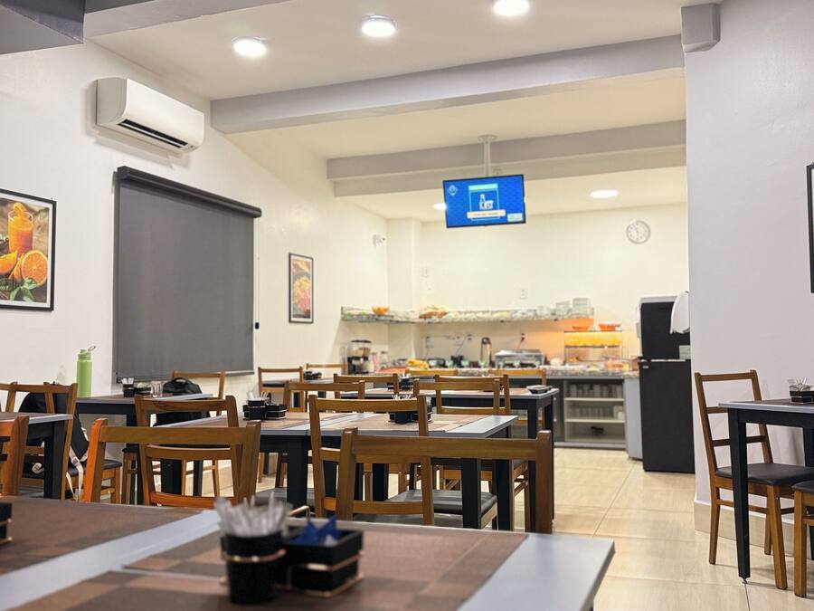 Un restaurante con varias mesas y sillas, un equipo de aire acondicionado y una pantalla digital con el menú.