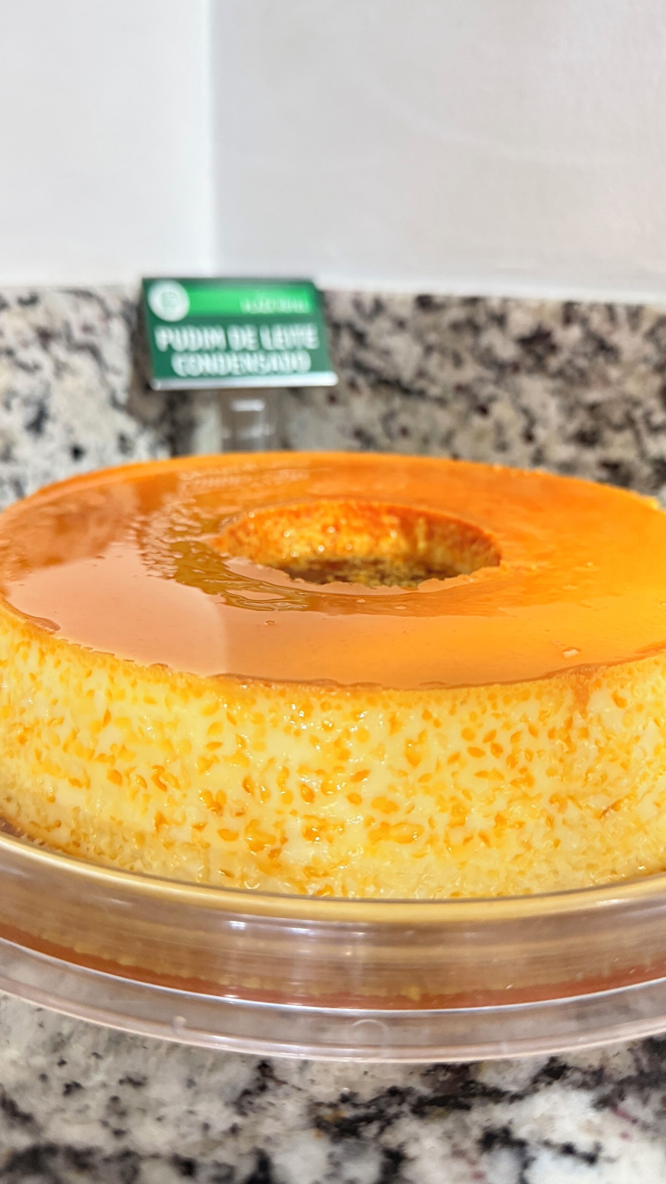 Um bolo de creme num prato de vidro transparente sobre uma bancada de granito.
