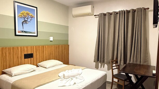 Habitación de hotel con cama, escritorio, silla, unidad de aire acondicionado y un cuadro en la pared.