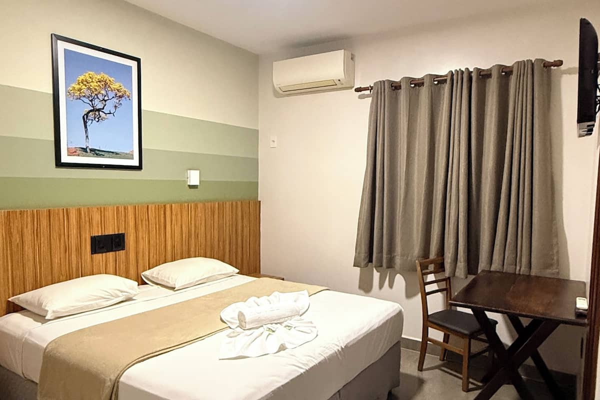 Une chambre d’hôtel équipée d’un lit, d’un bureau, d’une chaise, d’un appareil de climatisation et d’un tableau encadré au mur.