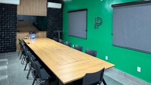Una sala de conferencias con una larga mesa de madera, sillas negras, una pared verde y paneles acústicos en el techo.