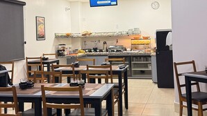 Comedor con mesas y sillas, una cocina al fondo y una pantalla digital con el menú.