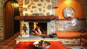 A stone fireplace with a fire, a wooden bench, and a stone wall with a circular mirror. - To Stefani tis Makrinas (Volos)