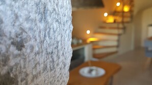 A stone wall, a wooden table with a white plate, and a staircase with warm lighting. - To Stefani tis Makrinas (Volos)