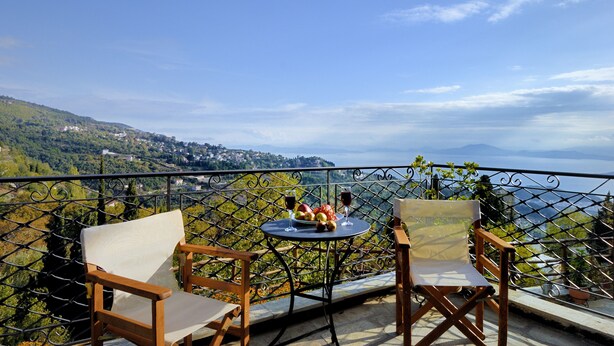 A balcony with two wooden chairs and a table with a fruit bowl and glasses of red wine. - To Stefani tis Makrinas (Volos)
