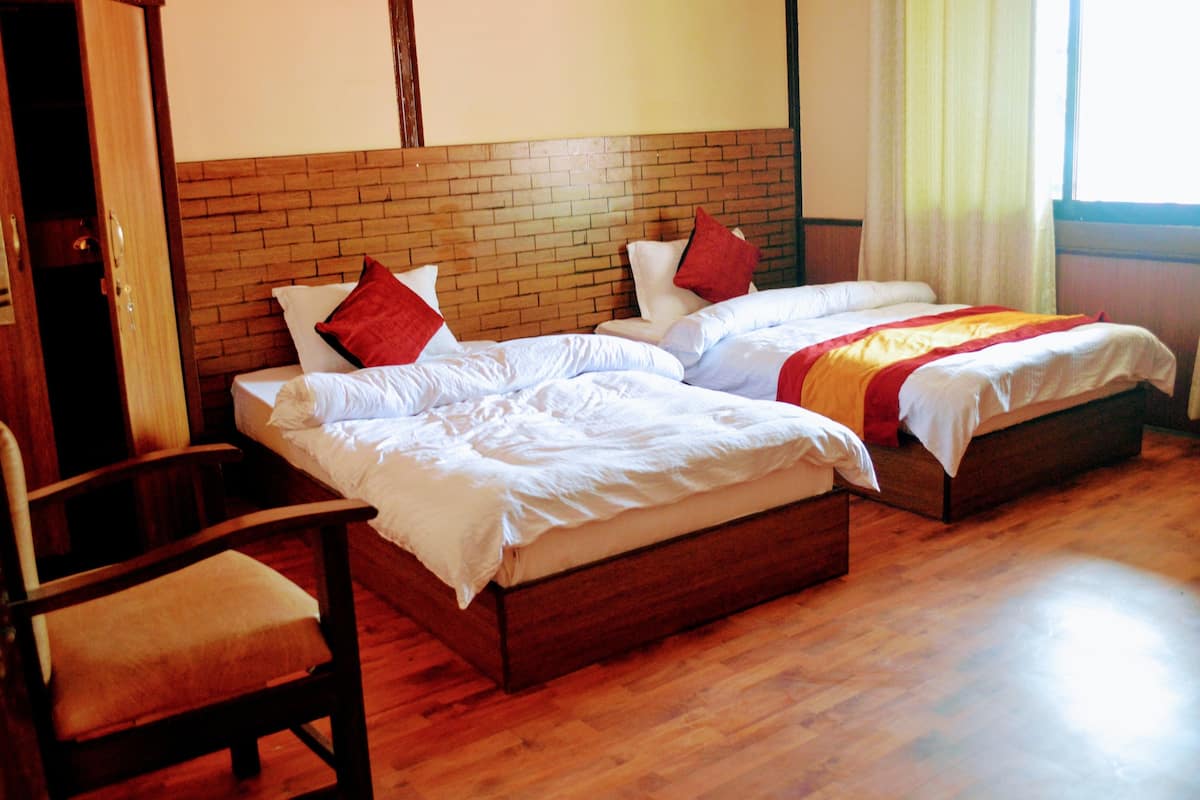A hotel room with two single beds, wooden headboard, and a wooden floor.