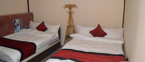Two single beds with white bedding and red pillows, a wooden headboard, and a woven chair.