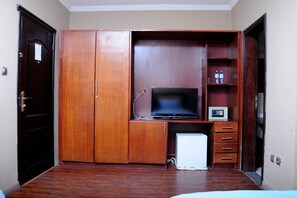 A compact room with a wooden wardrobe, a television, a small fridge, and a microwave.