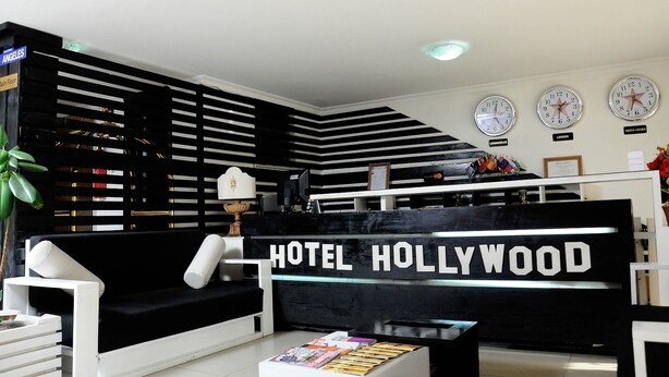 A reception area with a black reception desk labeled "HOTEL HOLLYWOOD," a chandelier, and three wall clocks. - Holly Wood Hotel (Addis Ababa)
