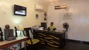 A reception area with a reception desk, a television mounted on the wall, a clock, and a sign indicating the reception. - Adna Hotel (Lagos)
