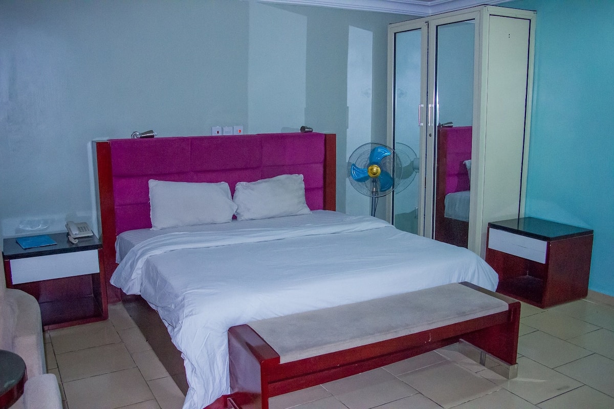 A bedroom with a bed, bedside tables, a fan, and a wardrobe.