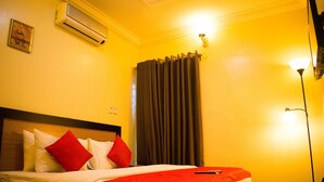 A hotel room with a bed, red pillows, a red blanket, an air conditioner, a curtain, and a nightstand with a lamp. - Esporta Suites (Lagos)