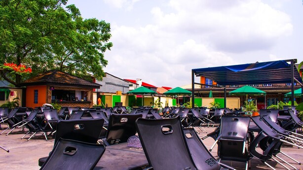 Rows of black lounge chairs and tables in an outdoor seating area with green umbrellas and a building in the background. - Esporta Suites (Lagos)