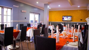 A dining area with tables set for a meal, chairs, and a television mounted on the wall. - Esporta Suites (Lagos)