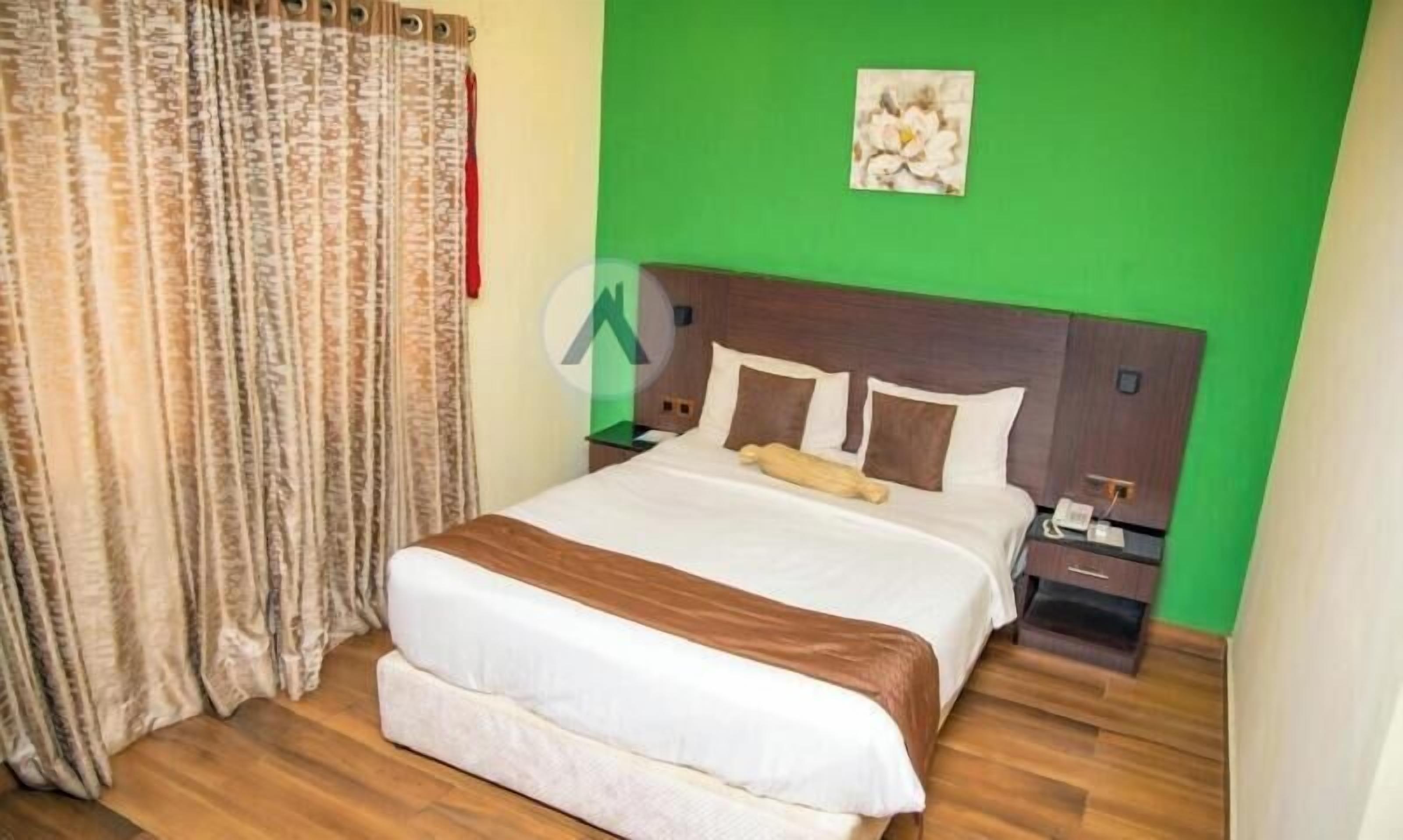 Una habitación de hotel con una cama grande, una mesita de noche y una cortina. La pared es verde.